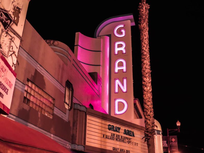 A neon pink and white marquee spelling GRAND vertically is lit against a black sky.