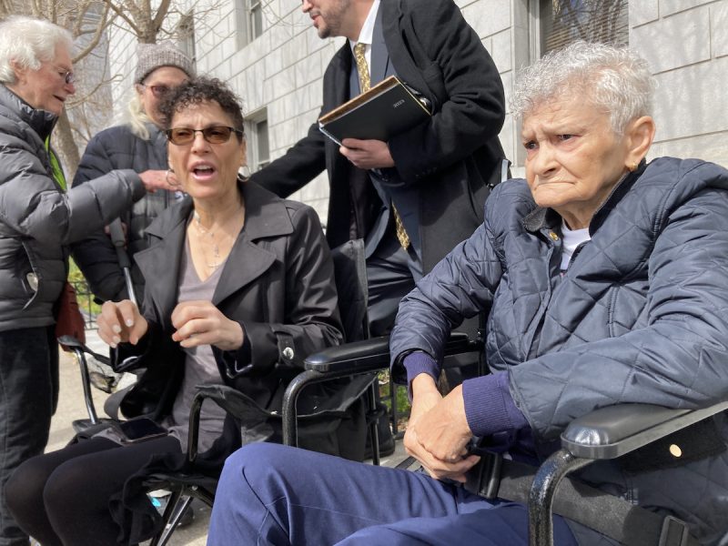Two women, one with dark hair and one with white hair, sit side by side.