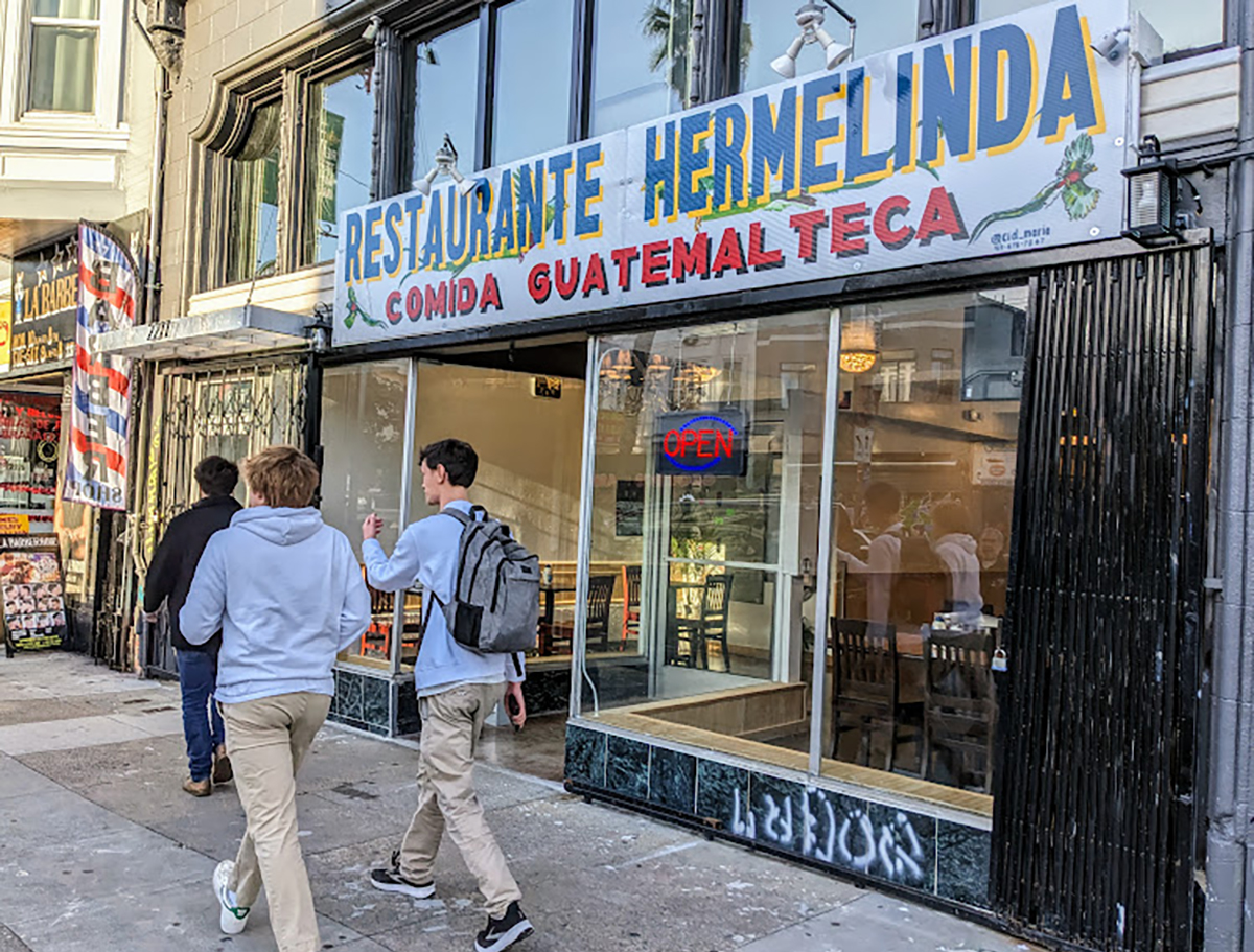 A restaurant front with two men walking by, their backs to the viewer.