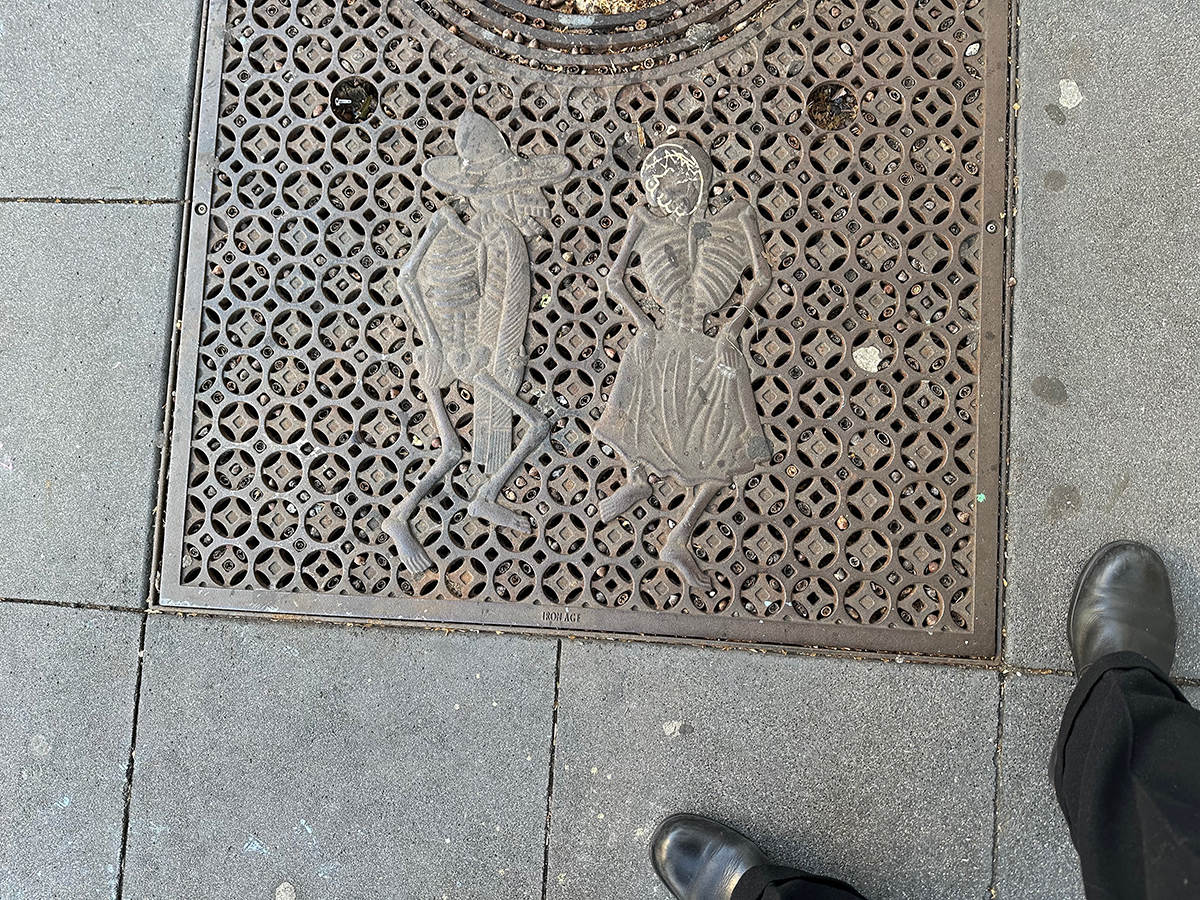 A tree grate embossed with skeletons. The woman has her face outlined in white.