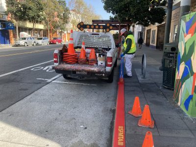 An SFMTA worker paints the curb red and blue.