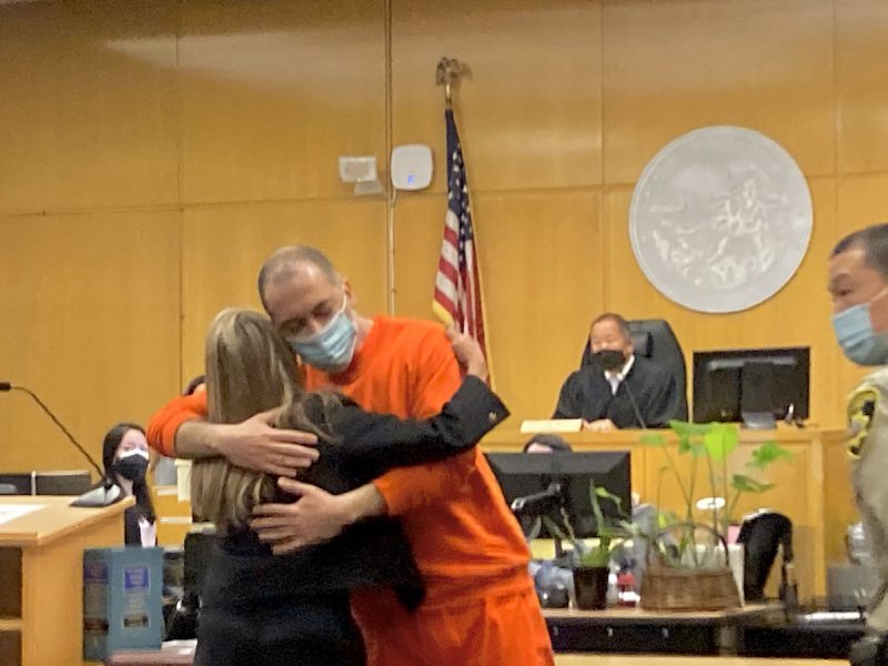 A man in orange sweats hugs a woman in a courtroom