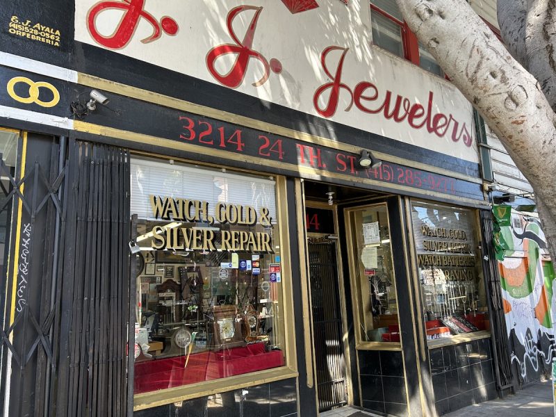 A black storefront with the words J J Jewelers painted on it. The windows propose watch and gold and silver repair.