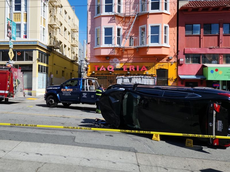 A flipped car sits behind police tape.