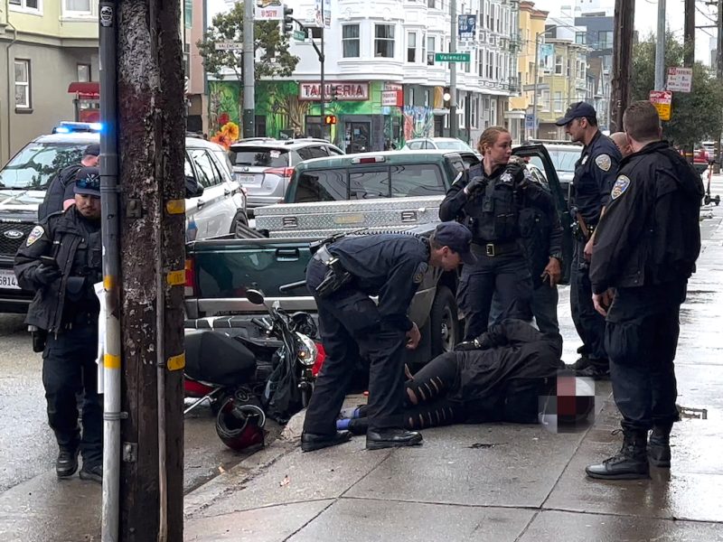 A Black woman handcuffed on the ground and surrounded by several San Francisco police officers.