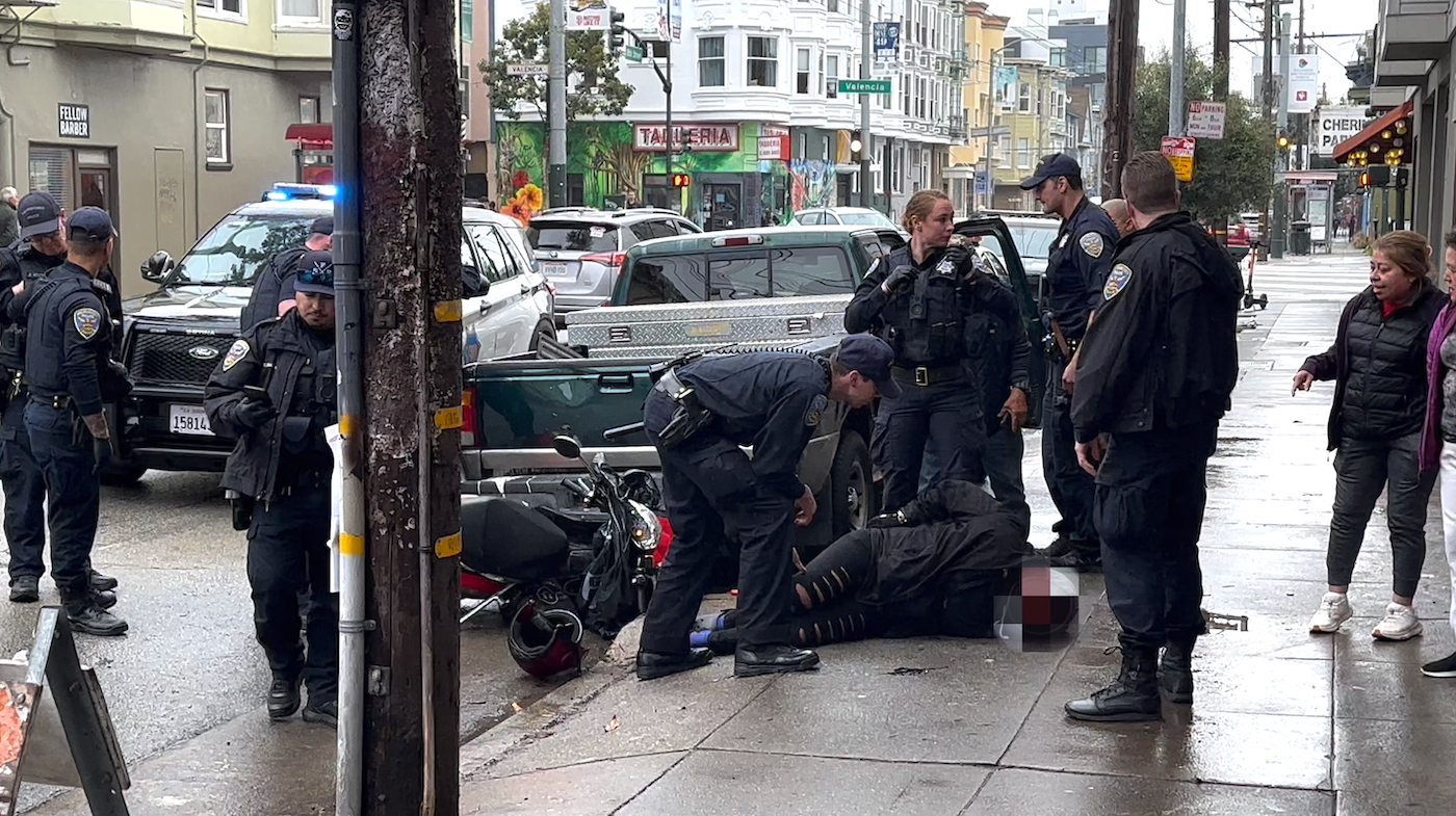 A Black woman handcuffed on the ground and surrounded by several San Francisco police officers.