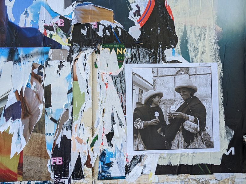 A board filled with wheat pasted flyers, many pulled off. One photo of two people remaining.