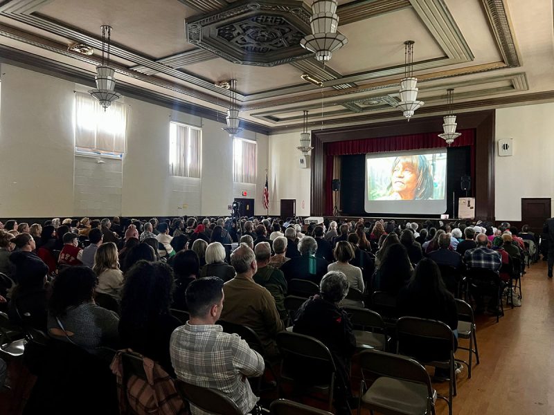 A hall full of people looking at a screen