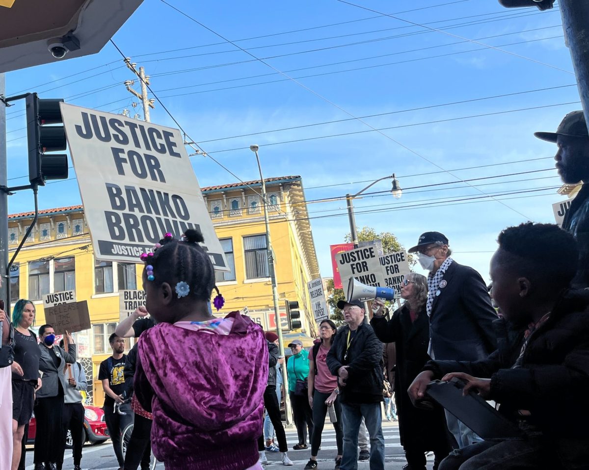 Little girl holding a sign saying "Justice for Banko Brown" in foreground, with crowd in background
