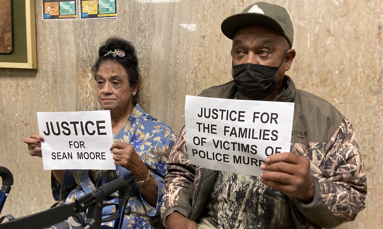 A woman and man hold signs that read "Justice for Sean Moore" and "Justice for the families of victims of police murder"