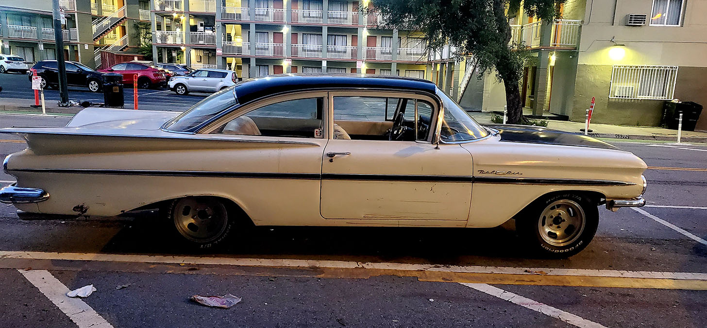 A long vintage car on the street, parked.