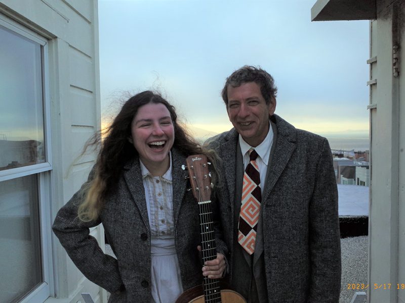 Two people standing outside between two buildings.