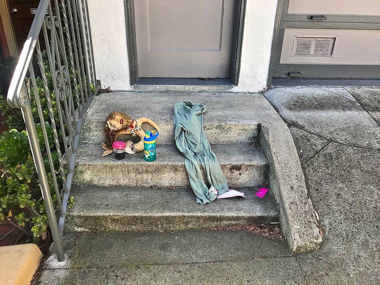 Pants and a stuffed mermaid toy on someone's front steps.