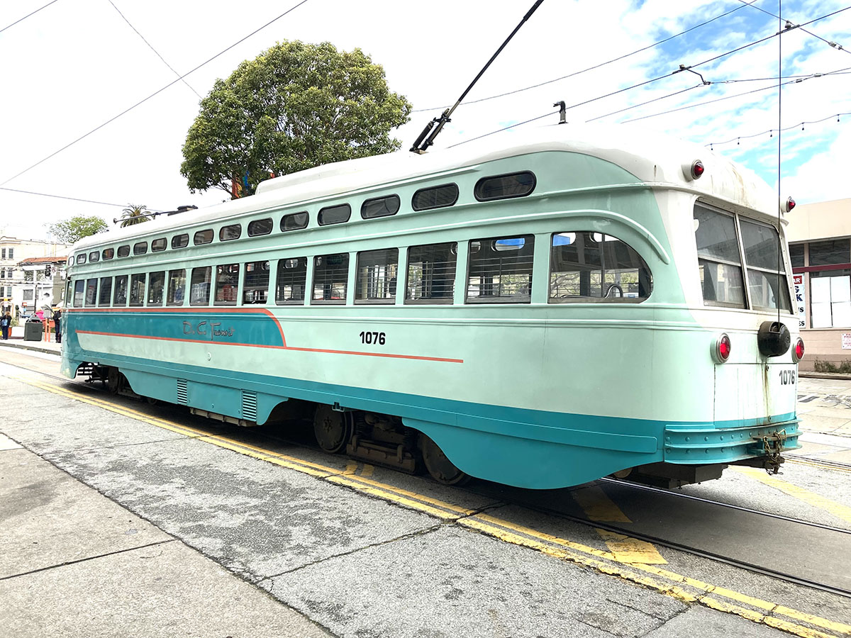 A long green streetcar with the. number 1076