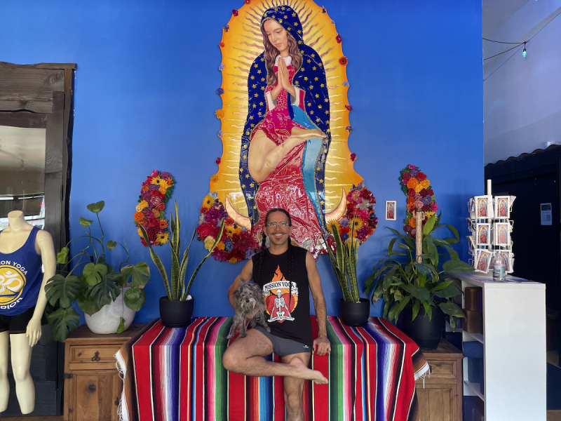 A man stands with a dog in front of a massive painting of Our Lady Guadalupe.