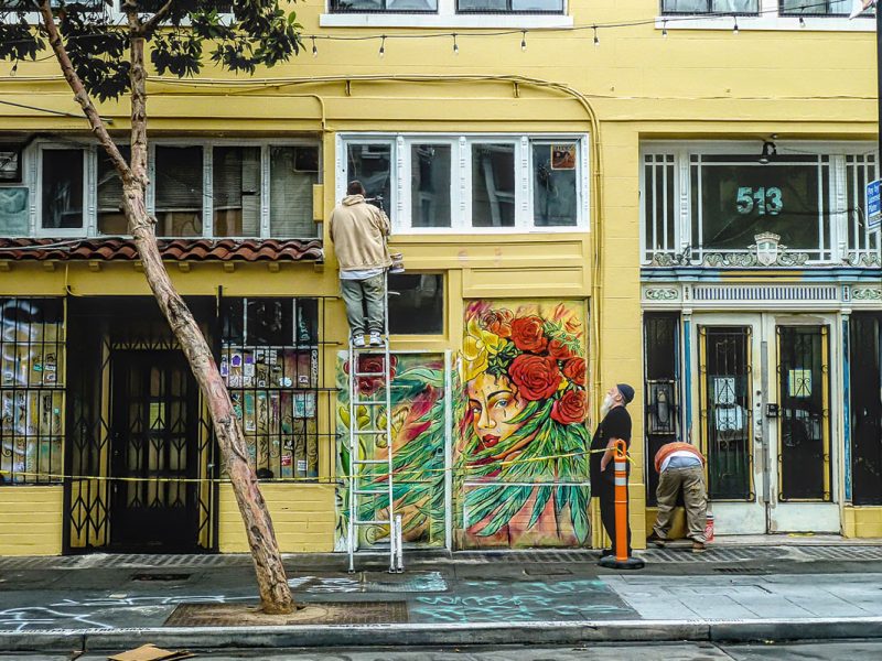 A man on a ladder set a against a yellow building.