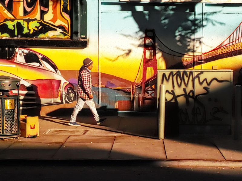 A man in a suit headed across a plaza, a mural in the background.