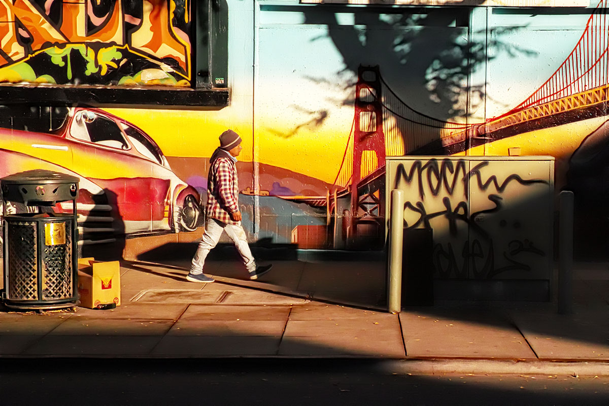 A man in a suit headed across a plaza, a mural in the background.