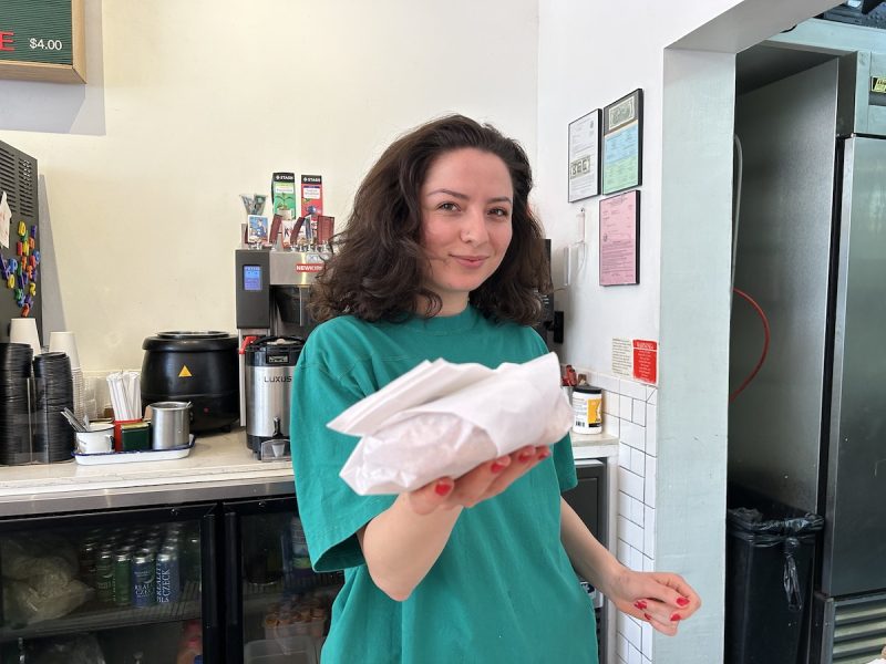A girl behind a counter holds out a breakfast sandwich.