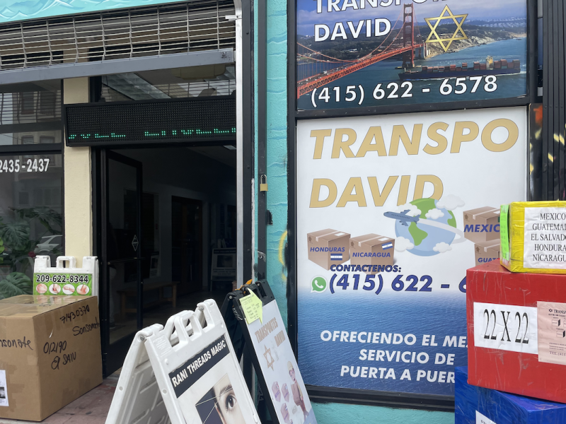 The storefront of Transportes David. There are colorful boxes representing the sizes of packages that can be sent. A sign in the window says to call 415- 622-6578 for shipping services to Mexico, Honduras, Nicaragua or Guatemala.