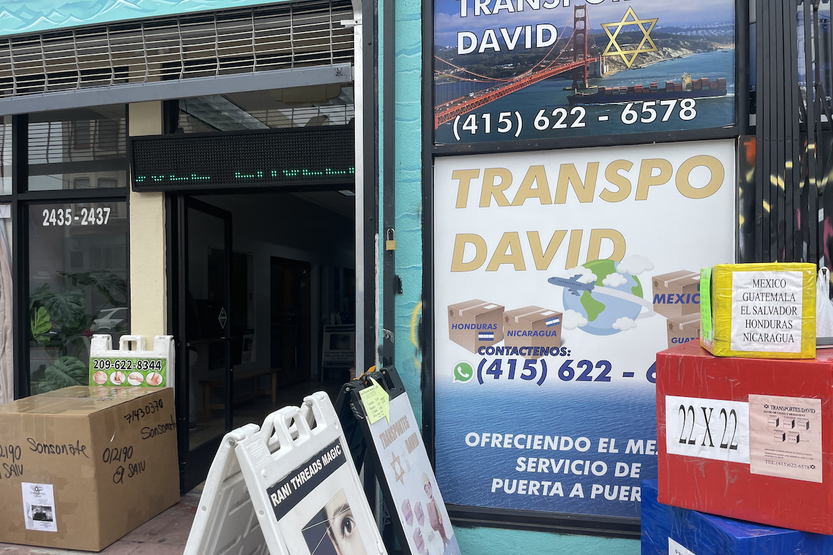 The storefront of Transportes David. There are colorful boxes representing the sizes of packages that can be sent. A sign in the window says to call 415- 622-6578 for shipping services to Mexico, Honduras, Nicaragua or Guatemala.