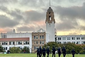 officers walking backs to camera on a park lawn in front of Mission High School in the background