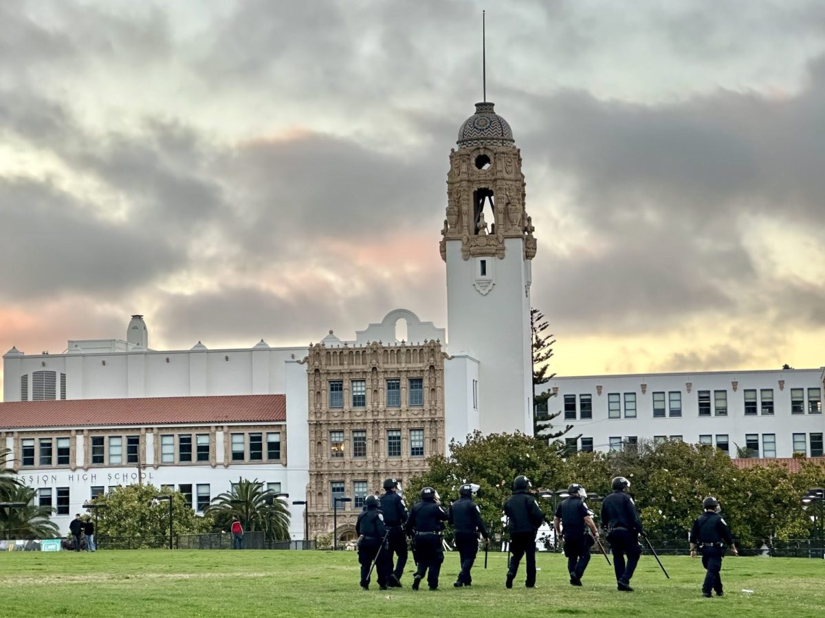 officers walking backs to camera on a park lawn in front of Mission High School in the background