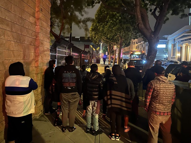 crowd of parents at the Dolores Park hill bomb with their back turns watch bus in distance