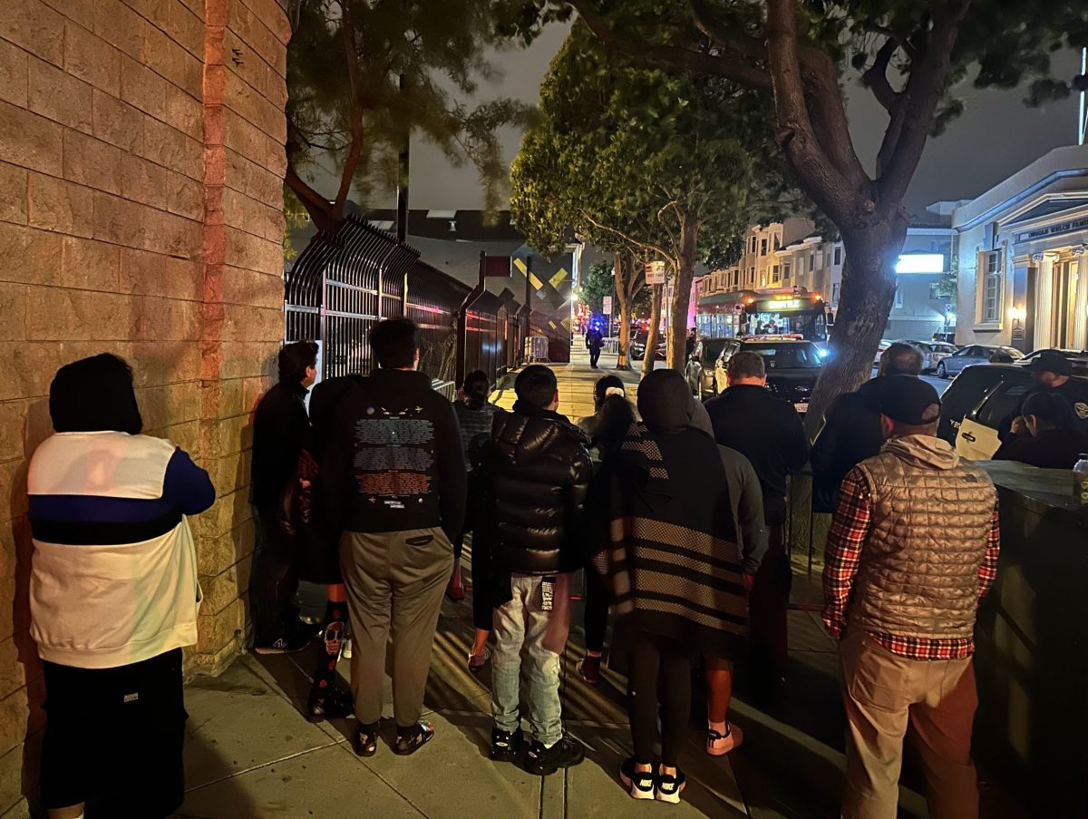 crowd of parents at the Dolores Park hill bomb with their back turns watch bus in distance