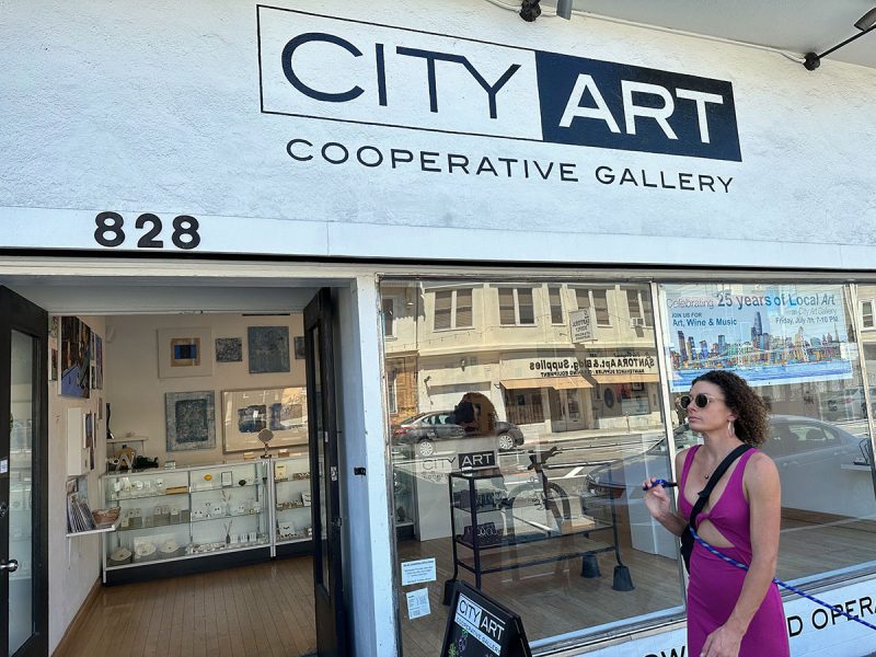 The front of an art store with the door open and a woman walking by.