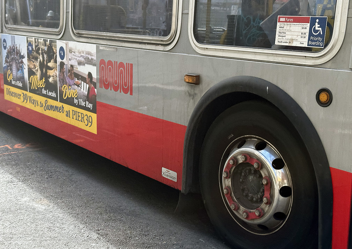 The side of a red and grey MUNI bus with one wheel and he bottom of some windows showing. Not the 22-Fillmore