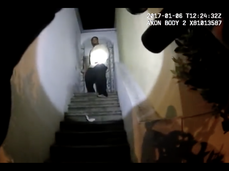 Gun points up staircase, toward a man in a spotlight standing in a doorway.