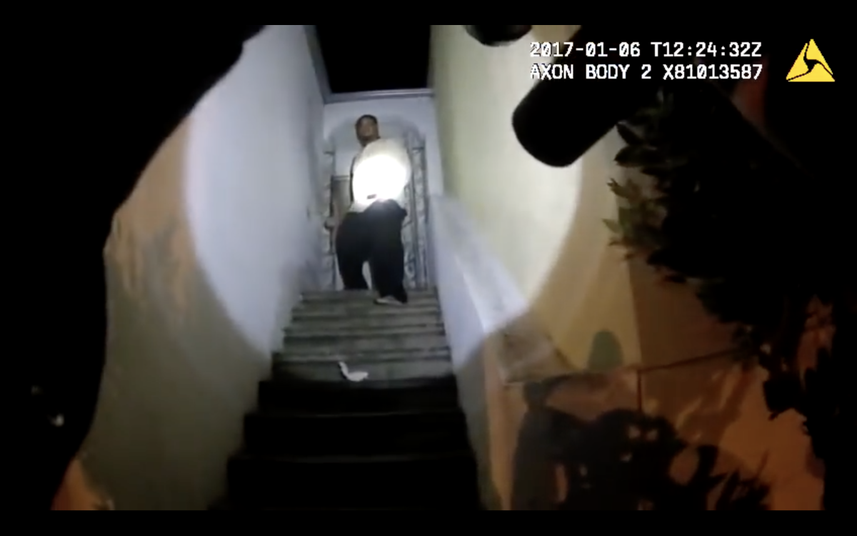 Gun points up staircase, toward a man in a spotlight standing in a doorway.