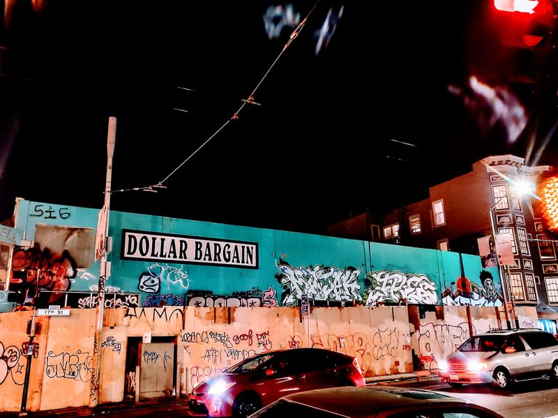 A store painted blue/green with boards in front of it. The scene is at night.