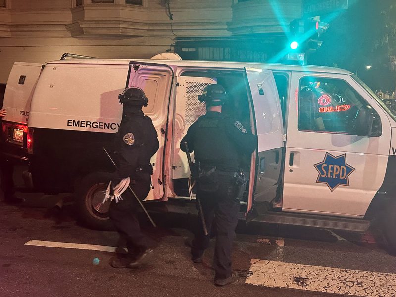 Two police officers standing next to a van in SF at night.