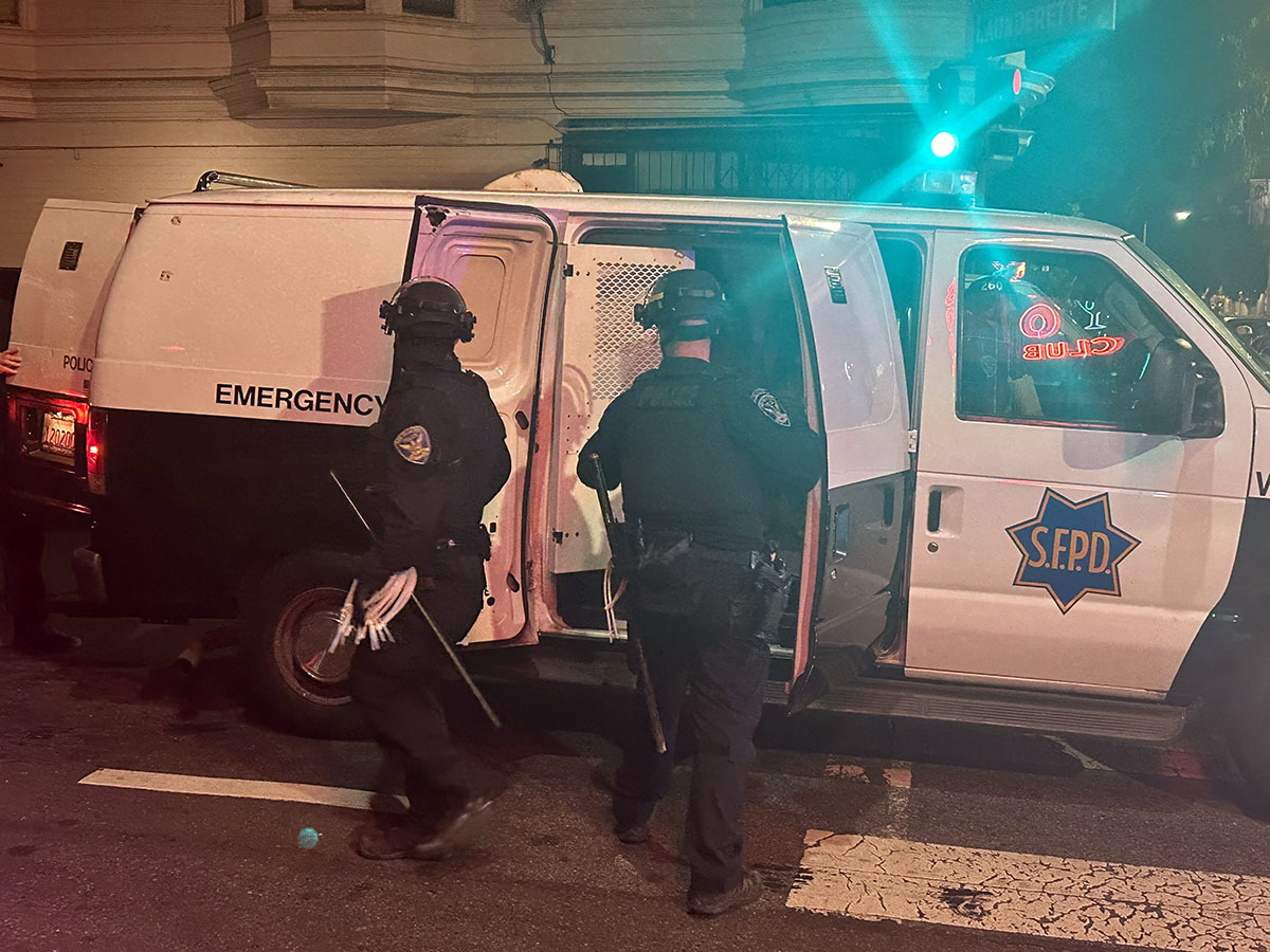 Two police officers standing next to a van in SF at night.