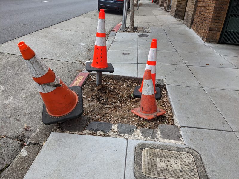 A triangle of three orange and white cones on a part of sidewalk being repaired.