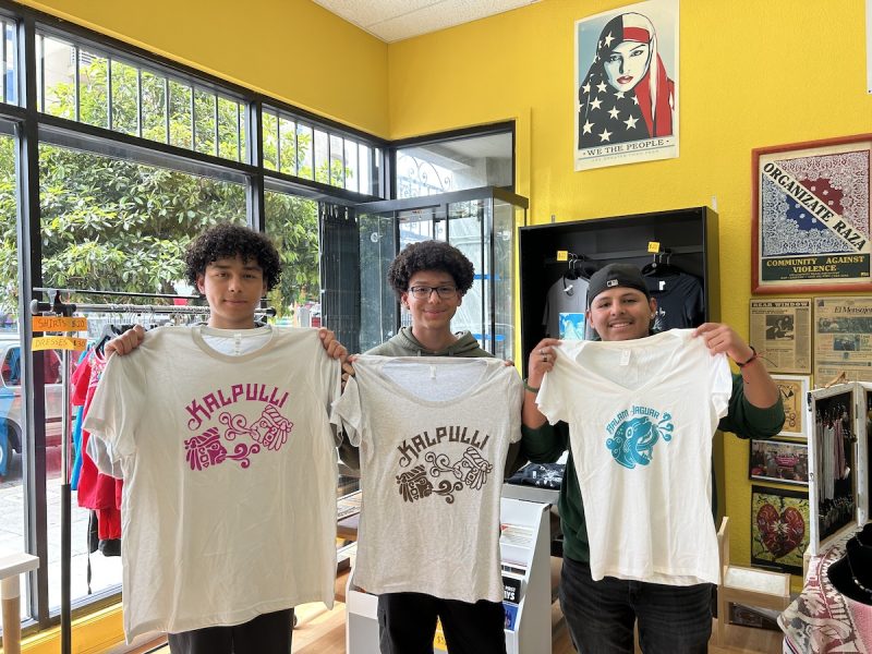 Three young Latino men pose and hold up white tee-shirts they plan to sell to fund a trip to Disneyland.