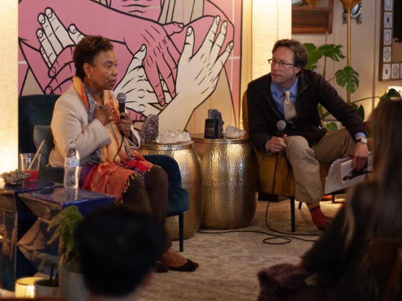 A Black woman and a white man with glasses on stage. The woman is speaking.
