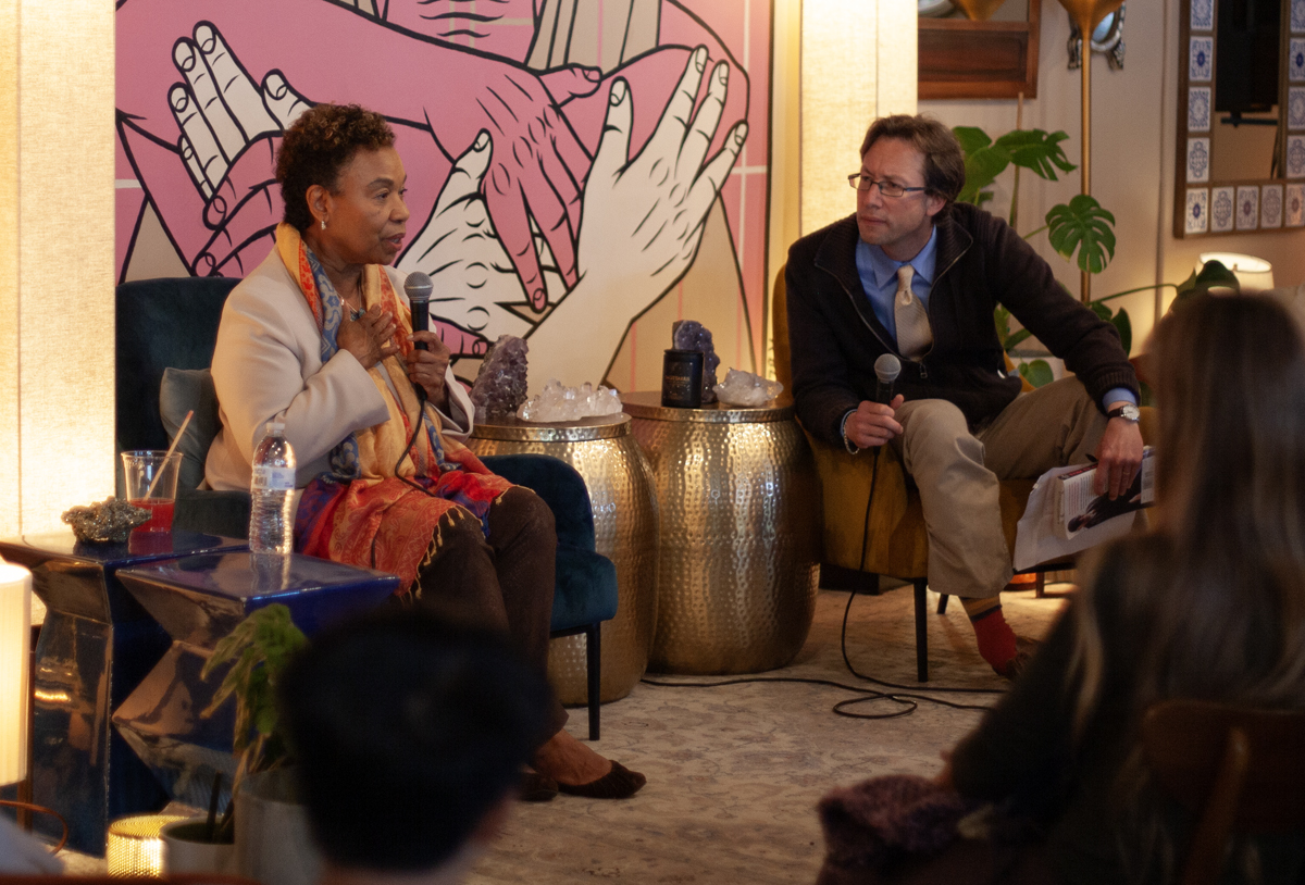 A Black woman and a white man with glasses on stage. The woman is speaking.