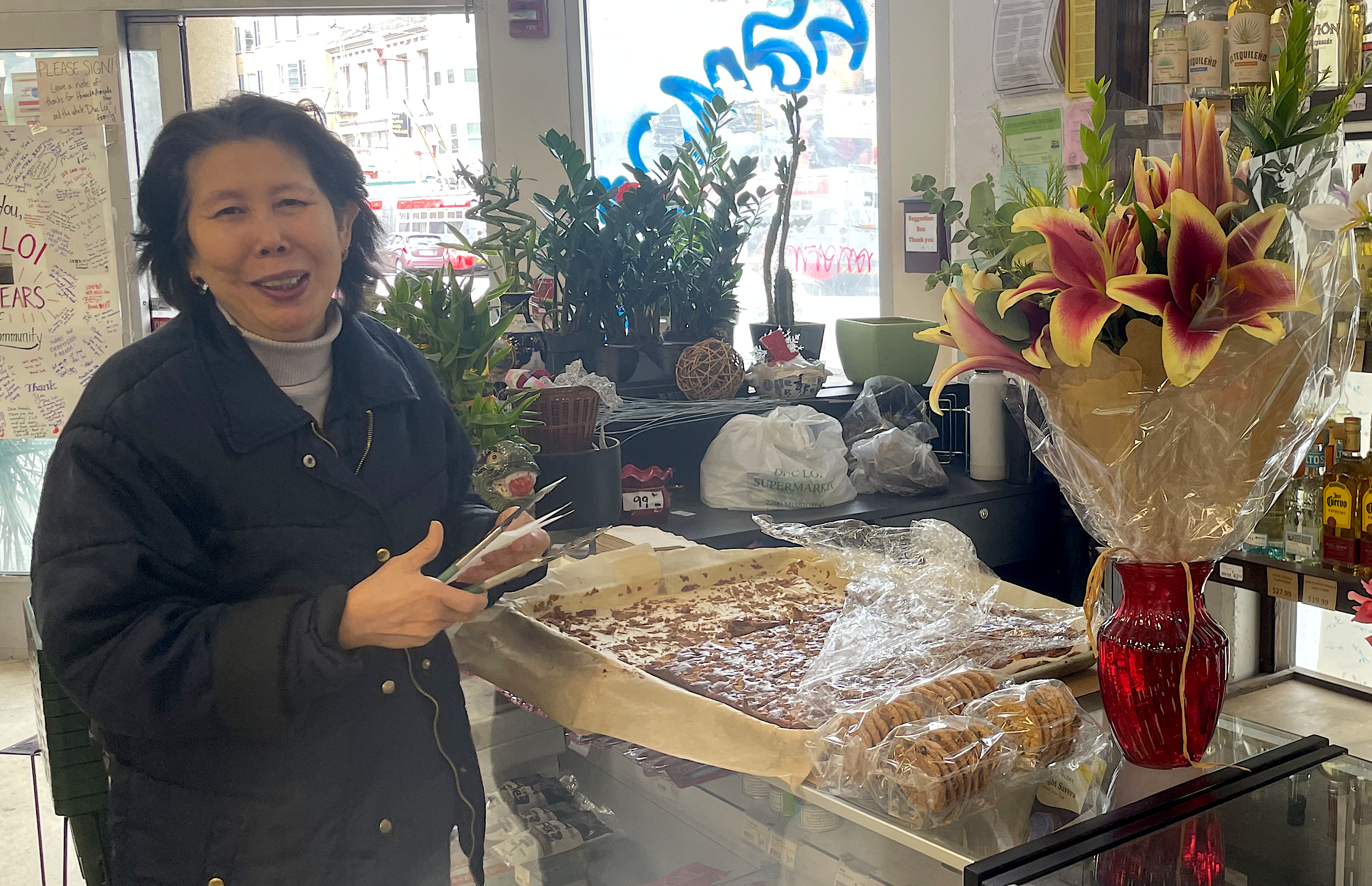 A woman stands by a table with a cake and a vase of flowers on it.