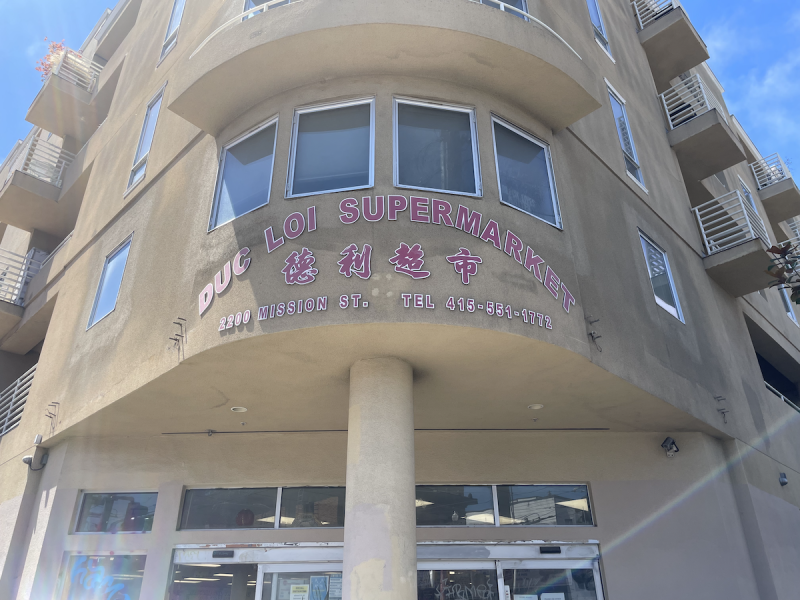 Duc Loi Supermarket , alongside Chinese characters, is on a storefront in red lettering.