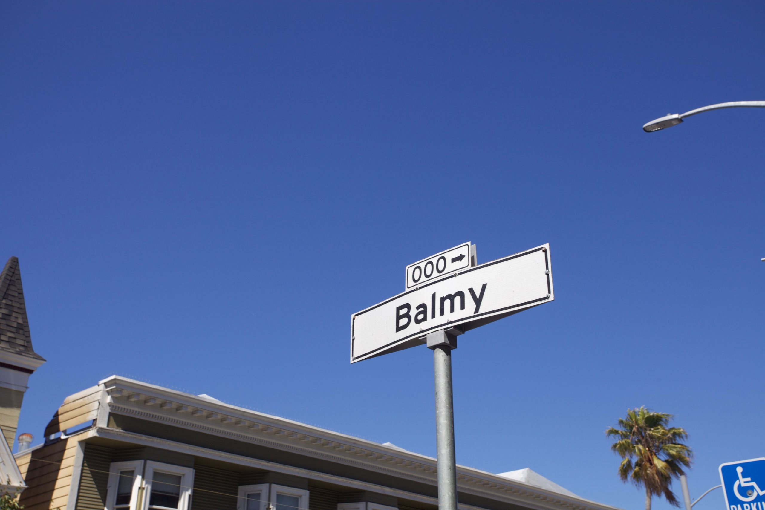 A blue sky, a palm tree and the top of a house and the street sign Balmy.