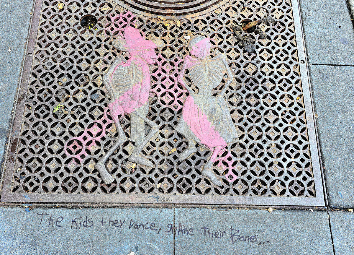 A metal grate showing two skeletons with some pink paint and the words below, the kids they dance.