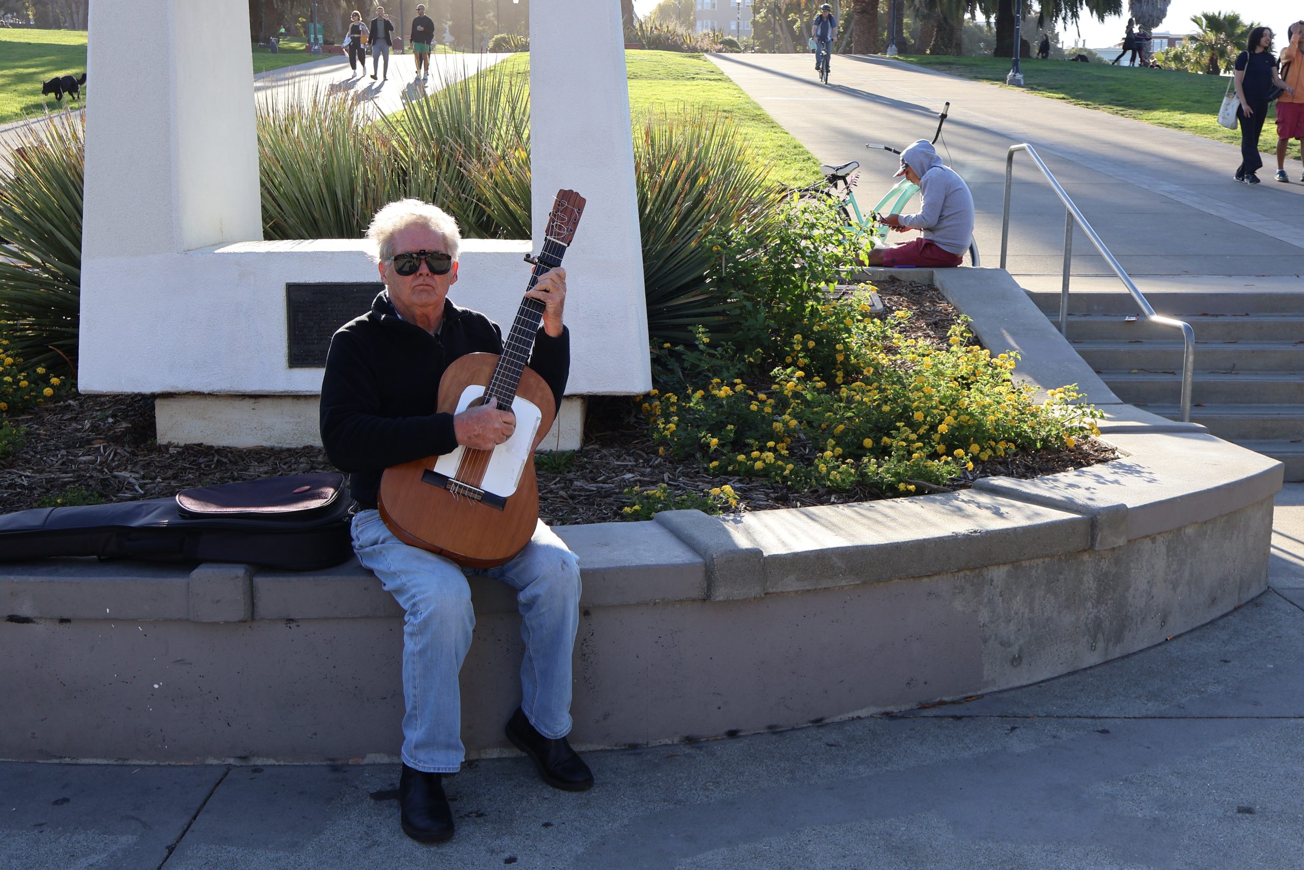A man sits with a guitar in hand at the bottom of the Mission Liberty Bell in Dolores Park.