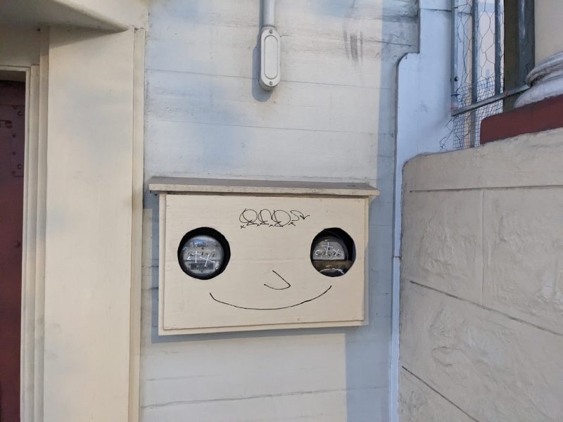 A face painted on a meter box on the wall.