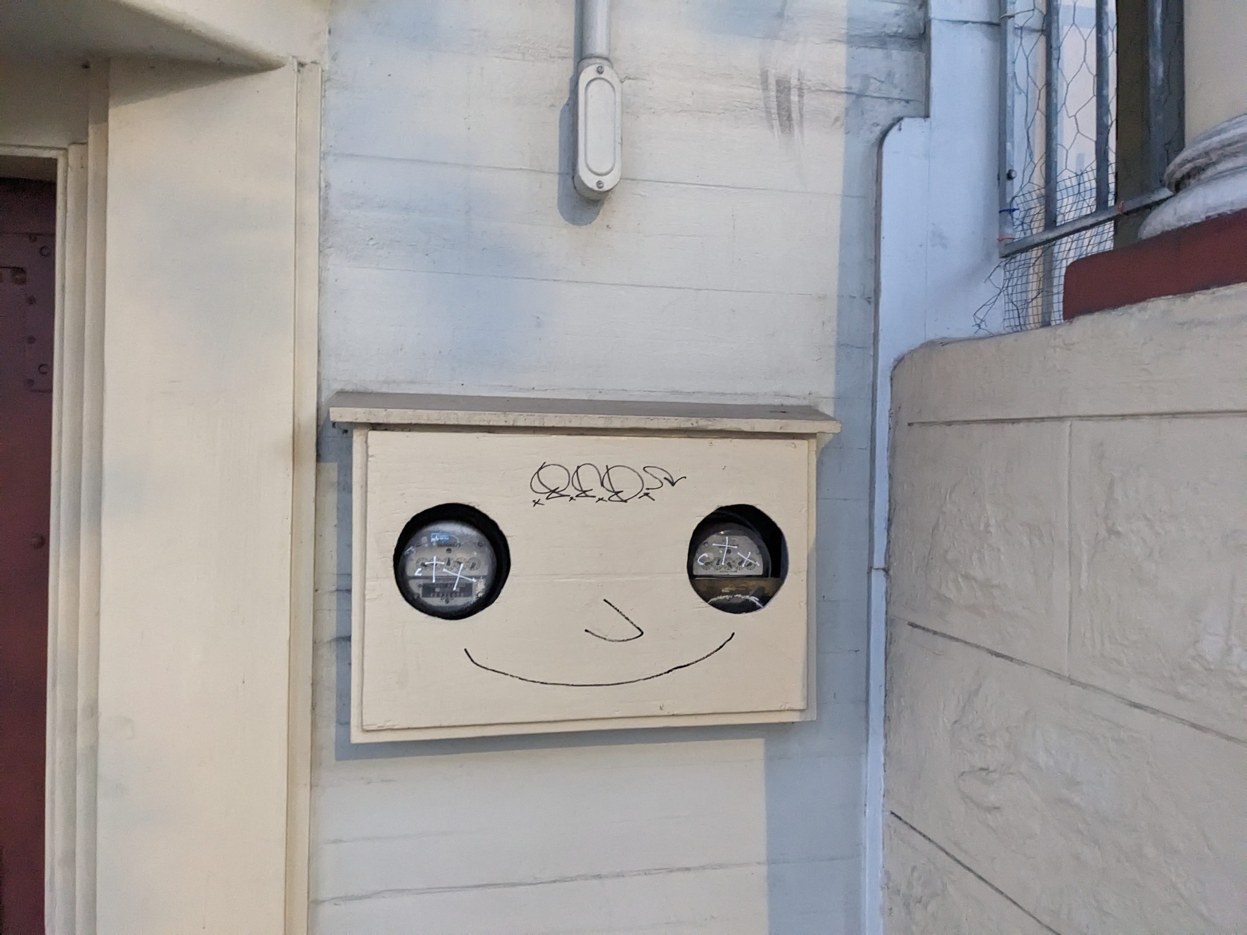 A face painted on a meter box on the wall.