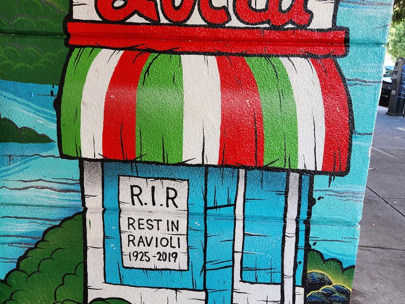 A mural of a storefront that has been closed, Lucca, in red with a red, green and white awning.