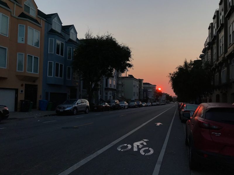Sunrise with an orange sun in the background and in the foreground a bicycle rider painted on the asphalt.