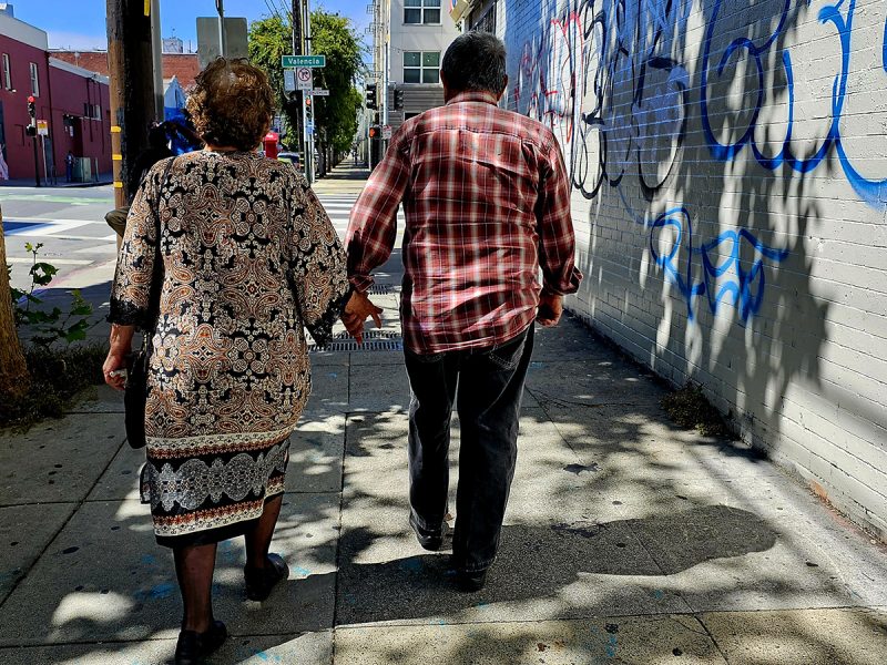 A middle aged couple from the back holding hands.